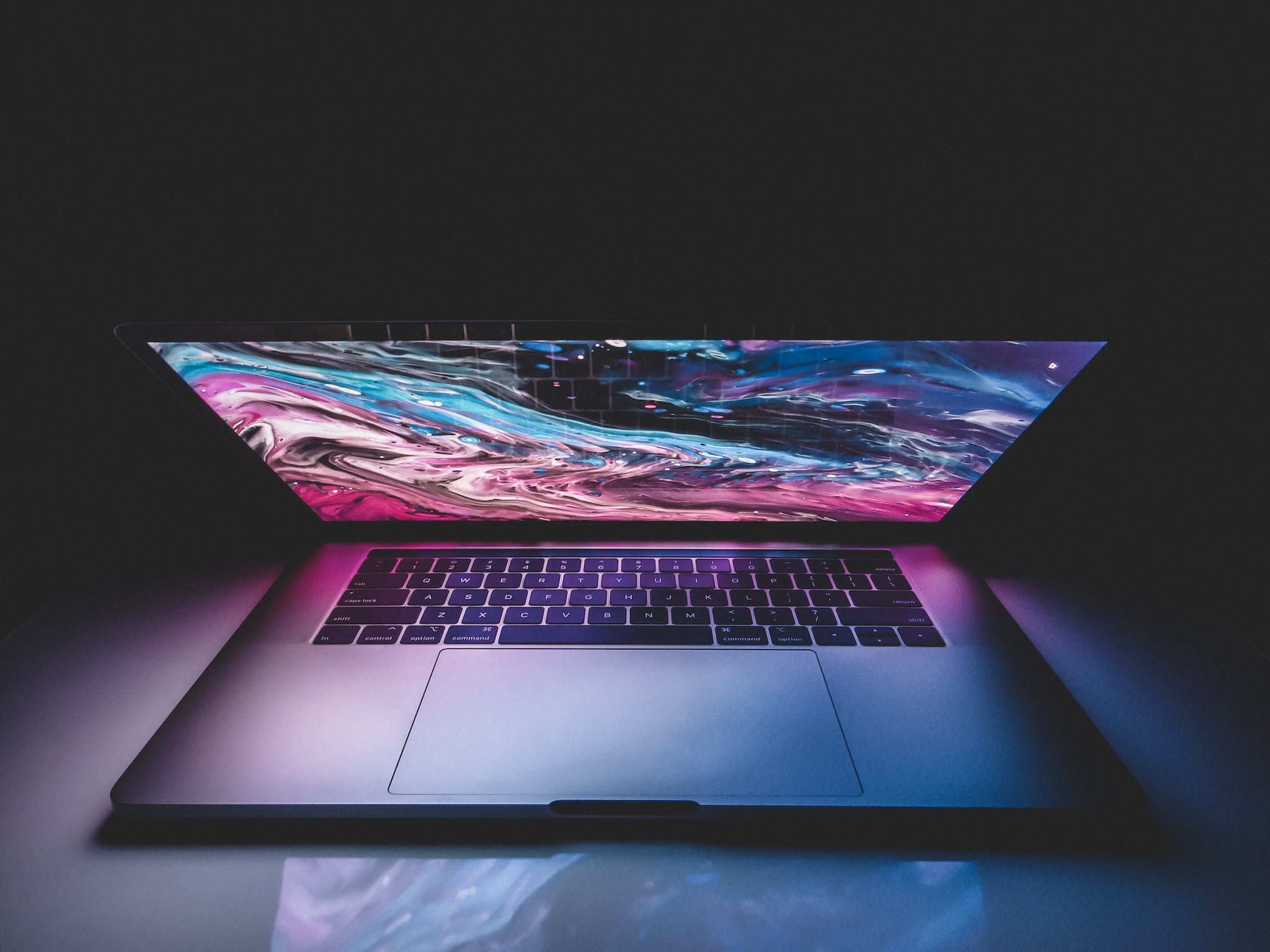 High angle of half opened modern laptop with colorful abstract picture on desktop placed on table in dark room